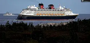 Disney_Cruise_Tips Disney Magic cruise ship sailing near a rocky coastline under clear skies