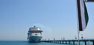 Dubai_India Cruise ship docked at a port in Dubai with the UAE flag flying high in the foreground.