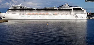 Msc_Cruise_Tips MSC cruise ship docked at a port, reflecting on calm water with a clear sky in the background.