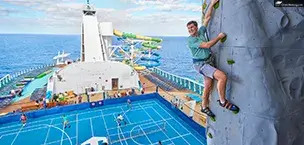 Royal_Caribbean_Cruise_Tips A smiling man climbs Star of the seas Rock Wall with the backdrop of a basketball court.