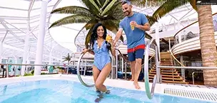 couple with drinks stepping into a pool onboard the Allure of the Seas cruise ship under a palm tree