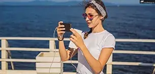 Royal_Caribbean_Cruise_Tips Woman using a mobile phone on a cruise ship, looking at vacation photos by the ocean.