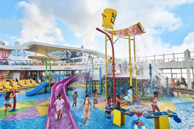 A wide shot of kids in Splashaway Bay, a water park, enjoying the water, running in the water, and yellow buckets with water spraying above them on Wonder of the Seas
