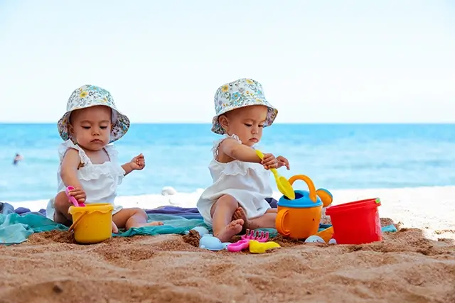 Sand toys are being played with by twin baby girls on a beach