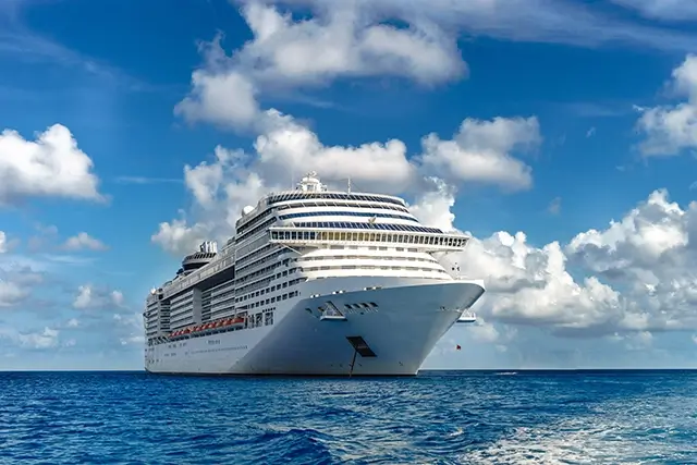 A cruise ship in crystal blue water with a blue sky in the distance