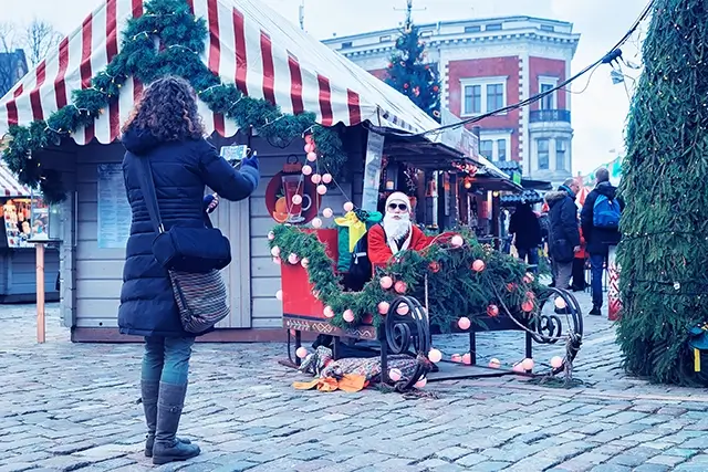 On Dome Square in the old town of Riga, a woman takes a picture of Santa Claus in a sled on a Christmas market