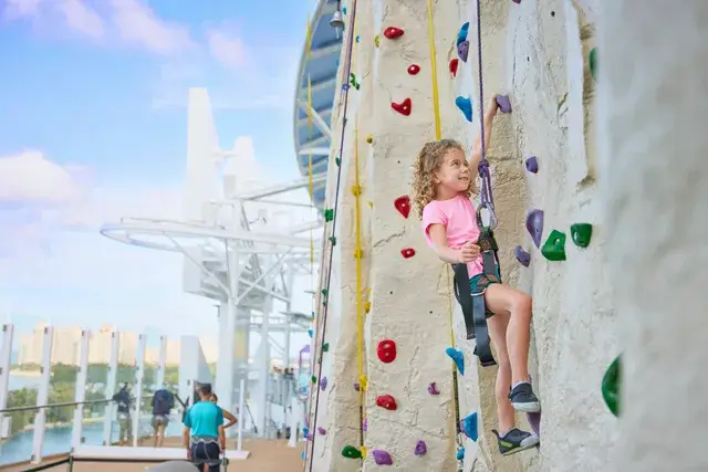 A young girl climbs up a rock wall named Adrenaline Peak, enjoying a challenge and having fun