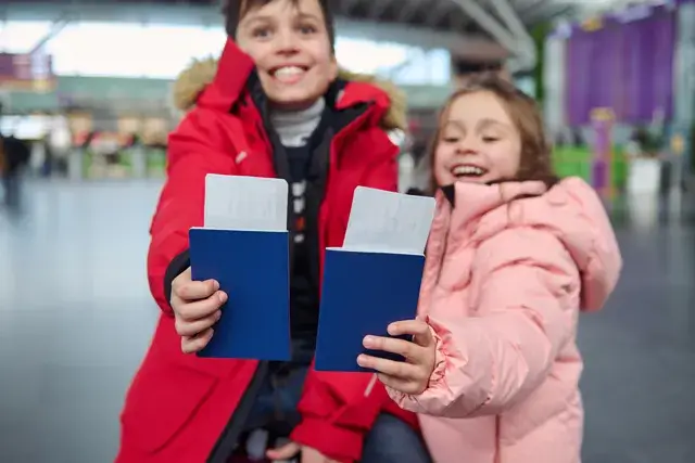 At international airport, two adorable european children hold passports, tickets, and boarding passes with toothy smiles. A family trip concept