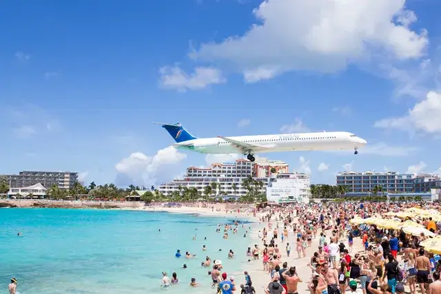 An airplane flying over Maho beach with a Saint Martin on it