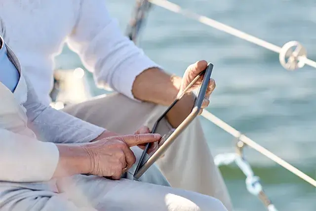 Sailing, technology, tourism, travel, and people concept - close up of a senior couple on a sailboat deck floating in the sea with a tablet computer