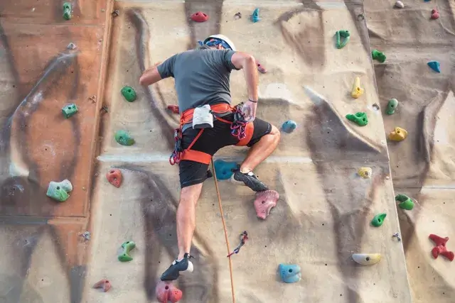 A young man practices rock climbing indoors on an artificial wall