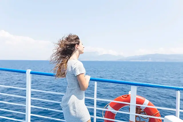 An attractive young woman stands looking at the blue sea from the ship's handrail