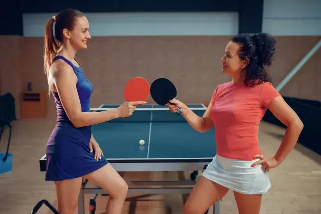 The two women are holding ping pong rackets