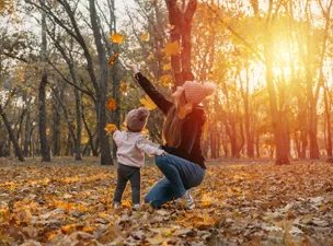 Mother and daughter tossing autumn leaves at sunset